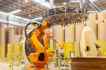 A robotic arm packaging large rolls of paper in a paper mill plant.