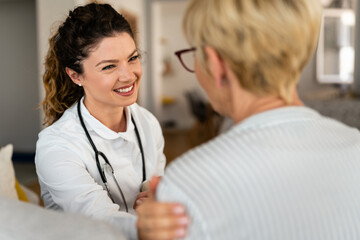 Happy smiling female doctor at home visit talking to unrecognizable senior blonde woman. Support,...