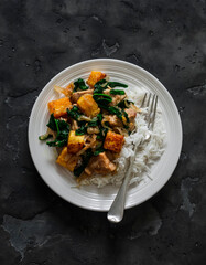 Slow cooker pork pumpkin spinach stew and rice on a dark background, top view