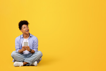 Joyful black male student holding cellphone and looking at free space