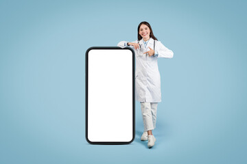 Young woman doctor with stethoscope pointing at giant phone blank screen