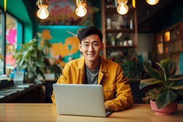 happy asian man sitting at table with laptop in cafe