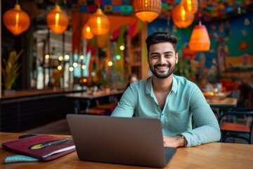 happy indian man sitting at table with laptop in cafe