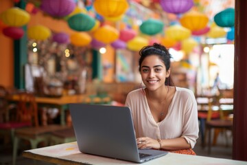 happy indian woman sitting at table with laptop in cafe