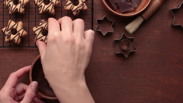 A human's hand places a homemade star-shaped cookie with chocolate in a wooden plate