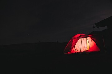 a red tent lit up in the dark at night in an outcropping - obrazy, fototapety, plakaty