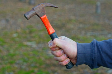 small, iron rusty old industrial with an orange handle dirty manual compact hammer for hammering nails in the hand of a worker on the street during the day