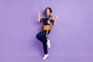 Full length body size photo of woman wearing overall gesturing like winner isolated on pastel violet color background