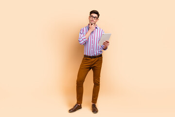 Fototapeta na wymiar Photo of minded man dressed stylish striped clothes use tablet ipad look up empty space offer poster isolated on beige color background