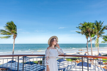 Woman with straw hat admiring view from oceanfront hotel terrace. Luxury travel and beachfront...