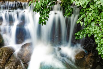 Long exposure shot of a cascading waterfall with a creek meanders through a lush forest - obrazy, fototapety, plakaty