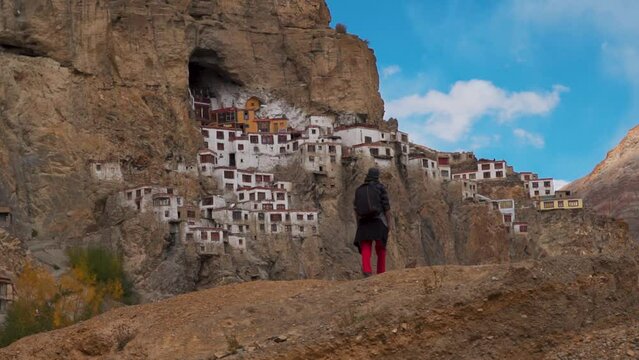 Defocused Indian man walking in front of the Phugtal Monastery made inside a cave in the mountain at Zanskar Valley in Ladakh, India. Man walking in front of remote Buddhist monastery in India. 