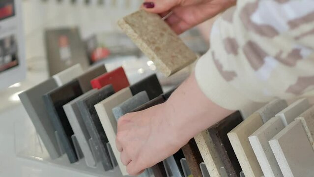 A woman examines samples made of artificial or natural stone, holding in her hands compares two colors. Makes a choice in a furniture store.