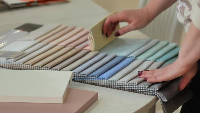 A woman's hand glides over samples of pastel-colored fabrics for upholstered children's furniture. Table of plain fabrics. The work of the designer decorator prop material selection.