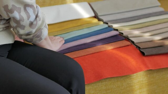 A woman is sitting on a yellow sofa looking at tissue samples, stroking with her hand, checking the softness. A table of solid colors of a sofa in a furniture store.
