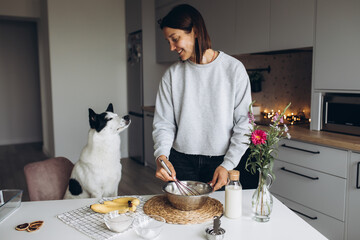 A cute big white and black dog helps her owner prepare a banana muffin with berries for breakfast. Friendship and healthy homemade food concept. Cozy atmosphere in the kitchen at home