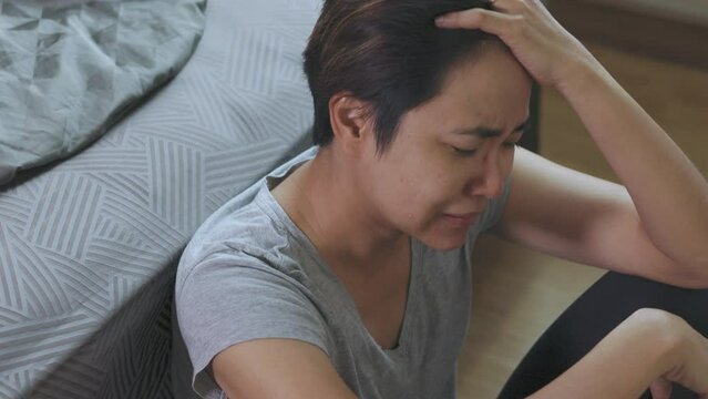 Close-up face of Asian woman who has suffered from abuse, violence, and the consequences of divorce, is seriously crying on bedroom floor, and expressing pain through heartbreak and despair.
