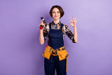Photo of young woman happy smile repairer hold perforator show okey alright sign isolated over violet color background