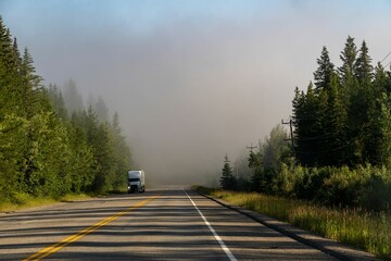 truck traveling down a road with smoke in the air and trees