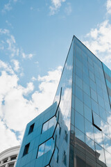 Abstract or graphic photo of the sky with clouds seeming to continue into a building with reflective squares of glass.