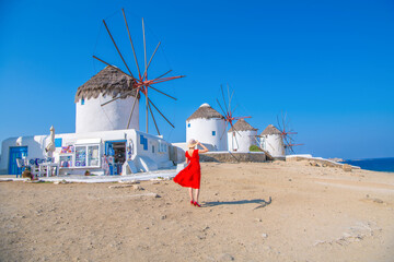 Woman in red dress at the windmills of old town Mykonos during a vacation in Greece, Little Venice Mykonos Greece - obrazy, fototapety, plakaty