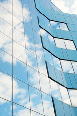 fragment of a skyscraper wall with mirrored glass against a sky with clouds. Glass wall. Close-up