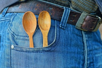 two old wooden small food empty clean table traditional classic yellow natural useful spoons in the side pocket of blue stylish fashionable jeans with leather brown belt