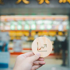 Businessman's hand holding a symbol Gold price graph upwards with blur gold shop background, concept of systems of raising or lowering Fed interest rates to correct inflation concepts.