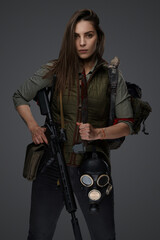 Naklejka premium Middle Eastern descent in post-apocalyptic survival gear, brandishing a dagger on a gray backdrop, showcasing her determination to survive