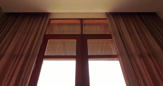 Heavy curtains closing automatically, low angle shot of top part of the window, looking from inside the room. Motorized curtain track installed in hidden curtain rod, ceiling edge is only visible