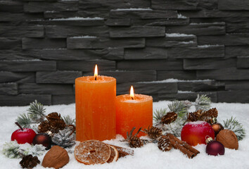 Obraz na płótnie Canvas Weihnachtliche Kulisse vor einer Steinmauer mit Kerzen, Zweigen, Nüße, Äpfel, Zimtstangen im Schnee mit Platz für Text.