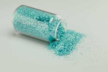 Jar of iridescent blue-green sparkles spilling out onto a white surface