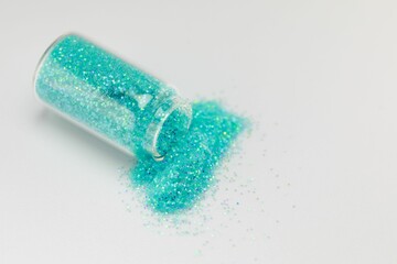 Jar of iridescent blue-green sparkles spilling out onto a white surface