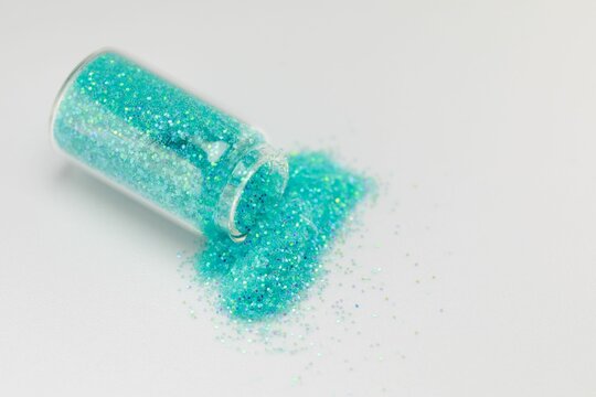 Jar of iridescent blue-green sparkles spilling out onto a white surface