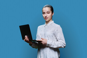 Serious teenage high school student girl using laptop on blue background