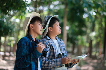Two young boys exploring the forest hiking and camping, learning about the wildlife, using binoculars to search for animals with friends. Happy smiling excited summer vacation.