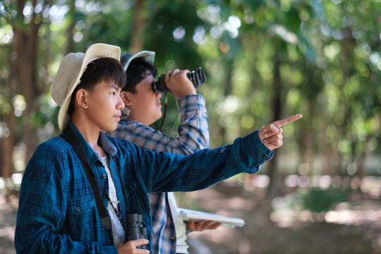 Two young boys exploring the forest hiking and camping, scouting, learning about the wildlife, using binoculars to search for animals with friends. Happy smiling excited summer vacation.
