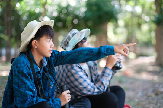Two young boys outdoors in the forest hiking and camping, scouting, learning about the wildlife, using binoculars to search for animals with friends. Happy smiling excited summer vacation.