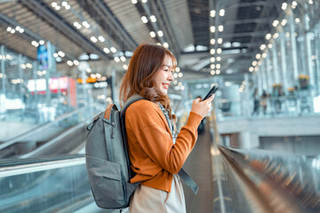 Asian tourist woman traveller with backpack using mobile phone while stand on moving walkway in...