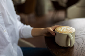Young woman holding a cup with cappuccino in hands