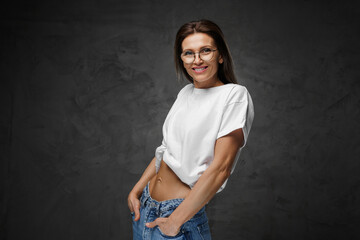 Obraz premium Radiant female in glasses and a white cropped tee proudly displays her toned core on a dark setting