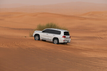White SUV truck driving on a large sand dune near Dubai, UAE at sunset hour, motion blur on the...