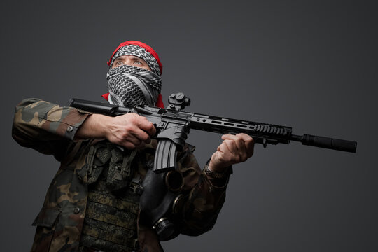 Middle Eastern radical fanatic soldier donning a white keffiyeh and camouflaged field uniform, armed with an automatic rifle, against a gray background