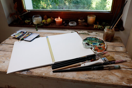 A watercolor workbook, brushes and paints - the artist's workplace near the window