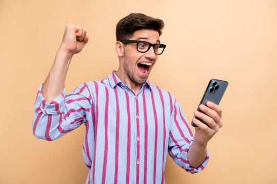 Photo of astonished funny guy received message on smartphone he raised fist up free spins bonus gambling isolated on beige color background