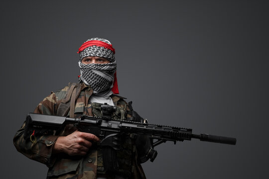 Militant from the Middle East, dressed in a white keffiyeh and camouflaged field attire, wielding an automatic rifle, set against a neutral gray backdrop - Powered by Adobe