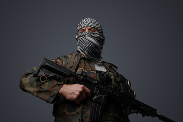 Middle Eastern radical fanatic soldier donning a white keffiyeh and camouflaged field uniform, armed with an automatic rifle, against a gray background