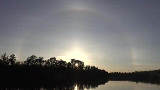 Unusual atmospheric phenomena. Very bright double halo (parhelic ring) over river at moment of evening sunset, windless spring day. Average flow of Don River. Mock sun with reflection in water