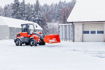 Red tracor cleaning snow in snowstorm. Blizzard weather conditions. Winter time street maintenance.