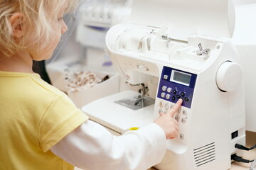 A little girl presses buttons on a cnc sewing machine.